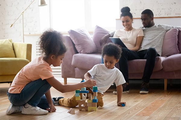 Children playing with blocks while parents sit on the couch nearby.