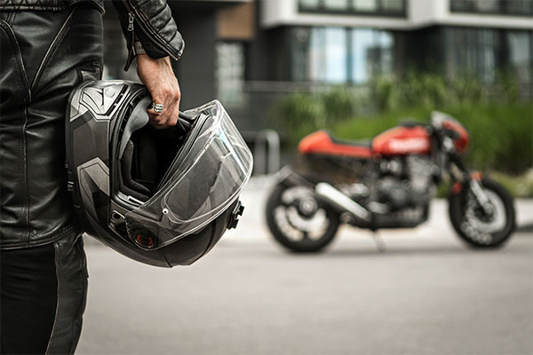 A rider holding a motorcycle helmet while standing near parked bikes.