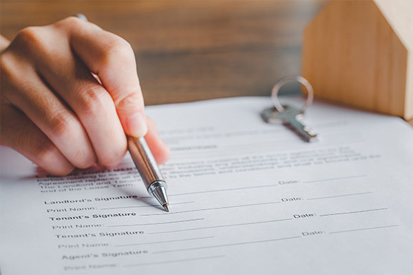 Person signing a document with a house key on the table.