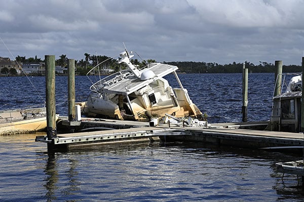 A partially sunken boat leaning at a dock on a cloudy day.