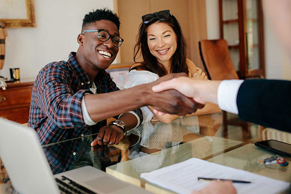 A smiling couple shaking hands with an insurance agent across a desk.