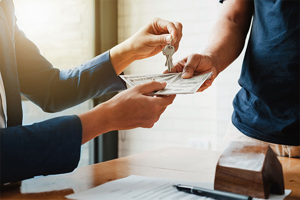 Two people exchanging a set of keys and cash at a table.