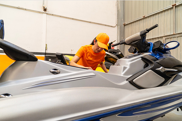 A person in an orange shirt inspecting a personal watercraft in a garage.