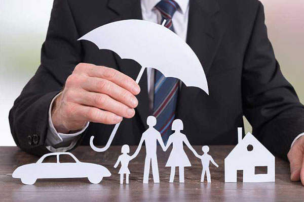 A person holding a paper umbrella over cutouts of a family, car, and house.